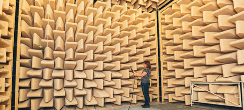 En kvinna står med ett ljudmätningsinstrument i ett rum med väggar i ljudabsorberande material.
