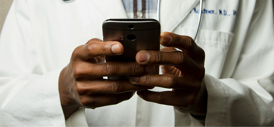 Person i rock med stetoskop håller mobiltelefon. Foto: Unsplash/National Cancer Institute
