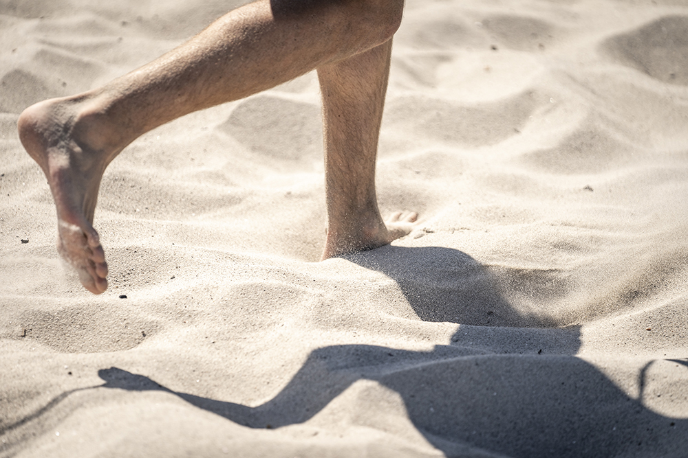 Bild av fötter på en person som promenerar på en sandstrand.