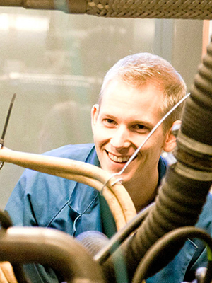 Young man sitting behind a machine and smiling to the camera.
