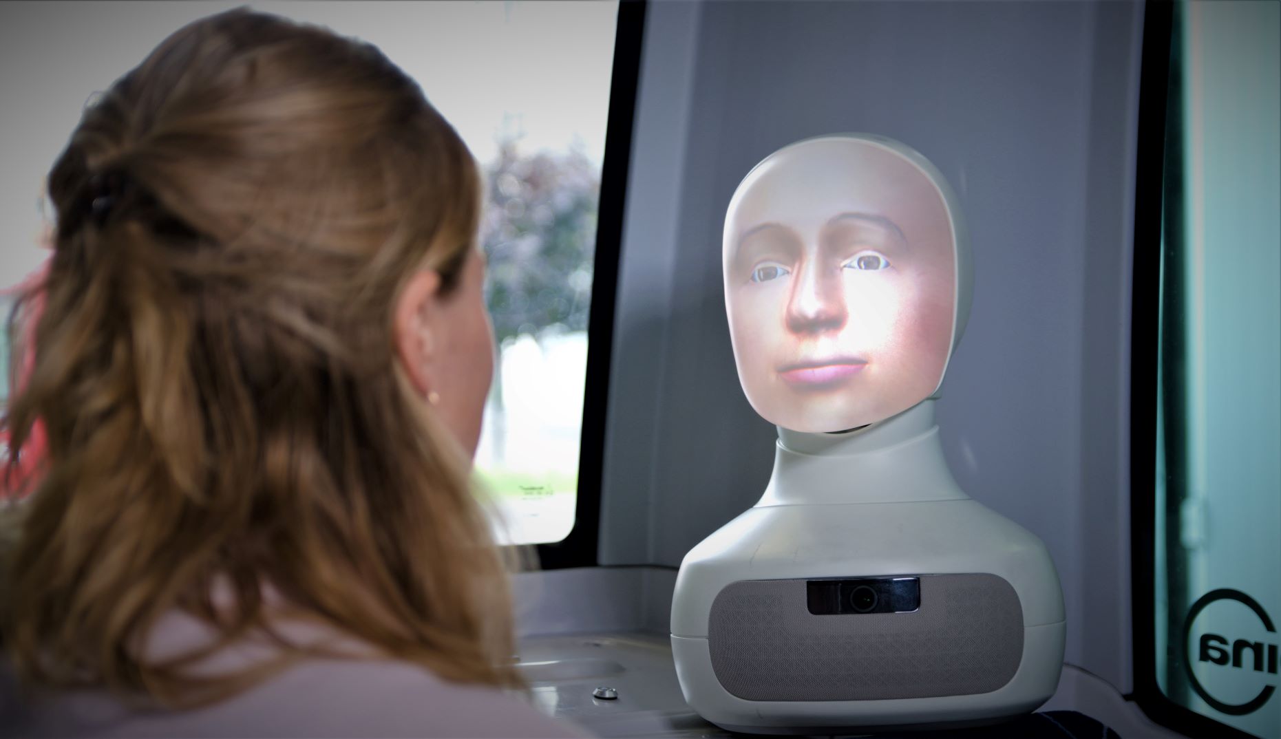 A social robot with neutral facial expression looking at a passenger in a driverless bus.