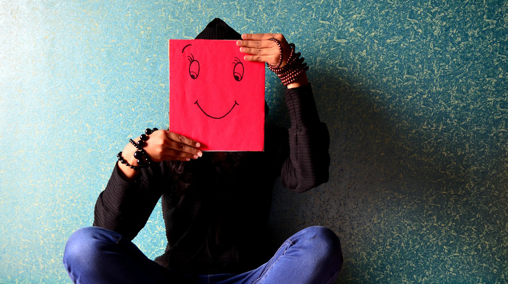 Person sitting alone with a Smiley-picture in front of her/his face. 