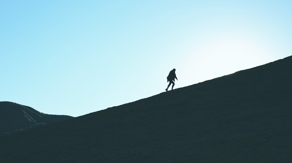 Man walking up a hill in counter light. 