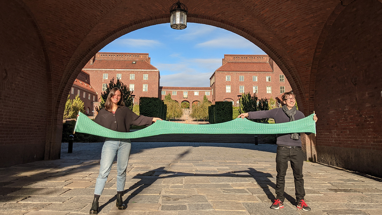 Nadia Campo Woytuk and a colleague holding up a knitted piece at borggården.