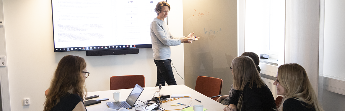 Picture of a meeting, one person presenting, four people sitting around a table. Photo: Olof Holdar