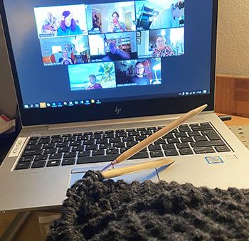 Photo: A laptop showing a video meeting and knitting on the table in the foreground.