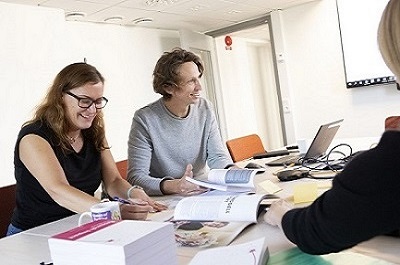 Two people sitting by a table, working and talking. Photo: Olof Holdar