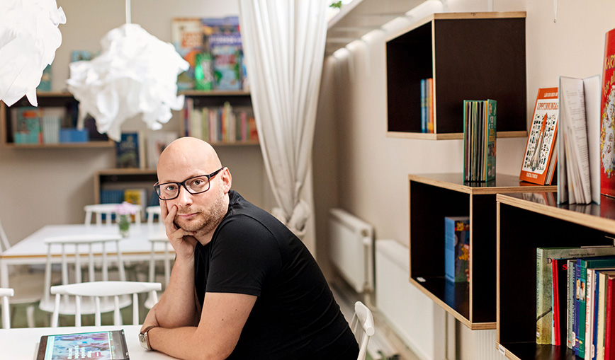 Stefan Stenbom sitting in front of a table. Behind him is a bookshelf.