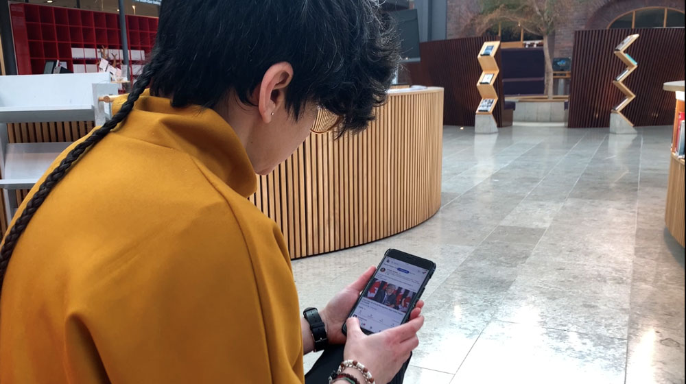 Person sitting in the KTH Library bent over her phone, LinkedIn.