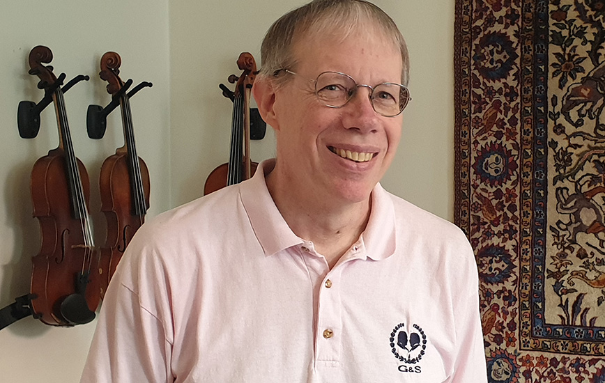 Portrait photo: A middle-aged man. Behind him on the wall hang three violins