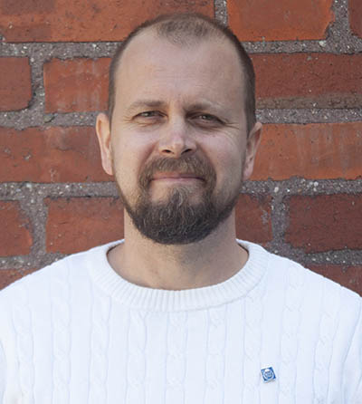 Portrait photo: A man wearing a white sweater in front of a brick wall.
