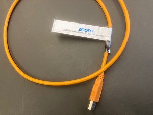Foto på en orange USB-kabel av typ USB-A, med en Zoom-etikett.