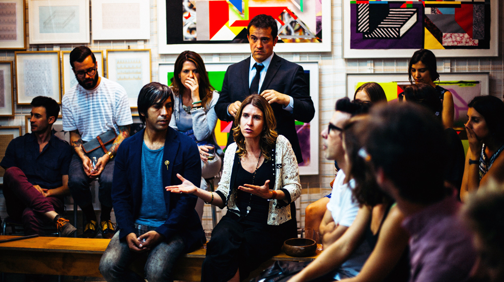 Group of people discussing. In the middle a gesturing woman, with the surrounding listening to her. 