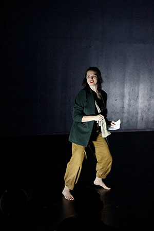 A dancer with beige pants and a black sweater in a dark room.