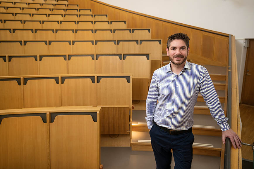 En leende man i ljus skjorta och mörka byxor som står i en tom föreläsningssal