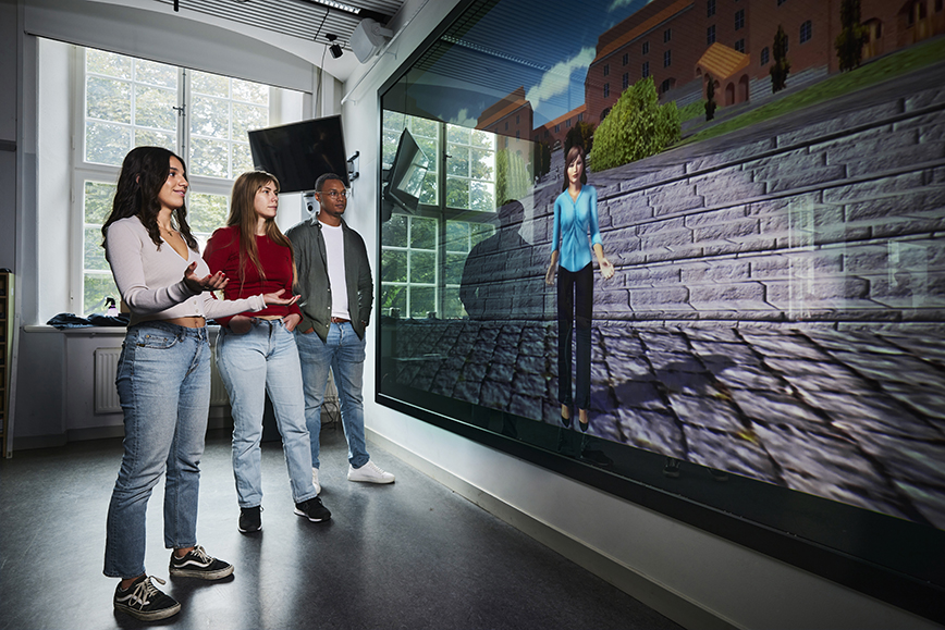 Three KTH students in front of a screen showing an interacting animated person