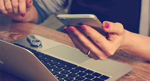 Computer and hand holding a phone. 