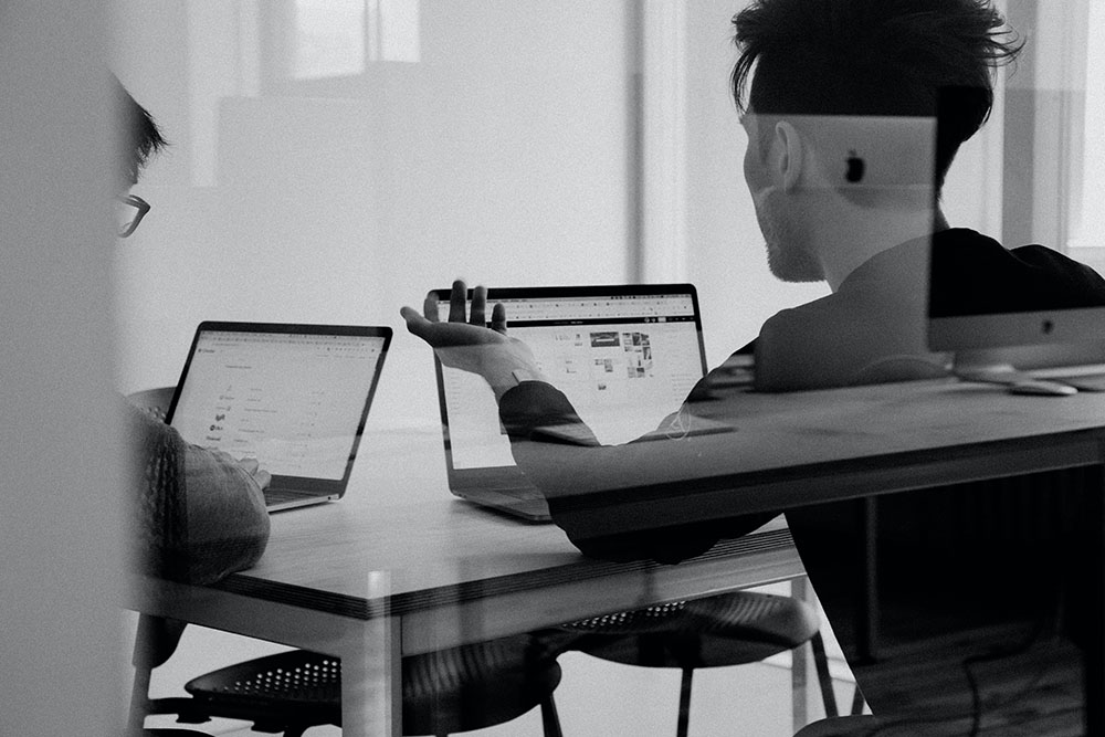 Två personer i kontorsmiljö vid varsin bärbar dator.