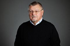 Foto: en äldre man i svart tröja och glasögon framför en grå bakgrund