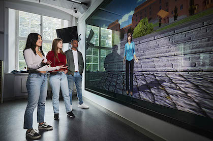 Three students looking at a huge screen showing a virtual picture.