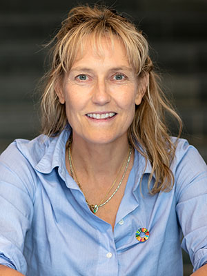 Porträttfoto: En leende blond kvinna i ljusblå skjorta.