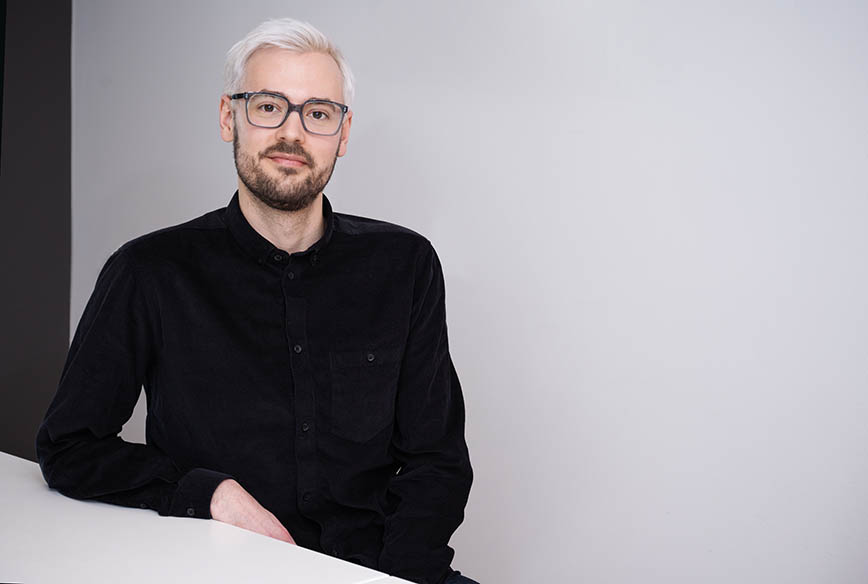 Portrait photo: a man wearing a black shirt in front of a white wall.