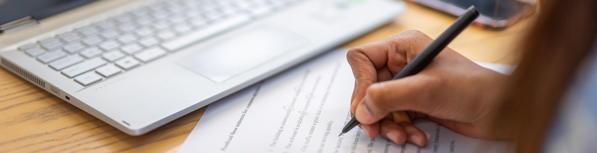 A hand writing on a paper and a keyboard to a laptop.