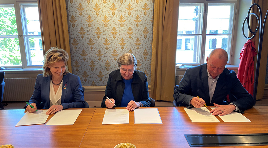 Three persons signing an agreement.