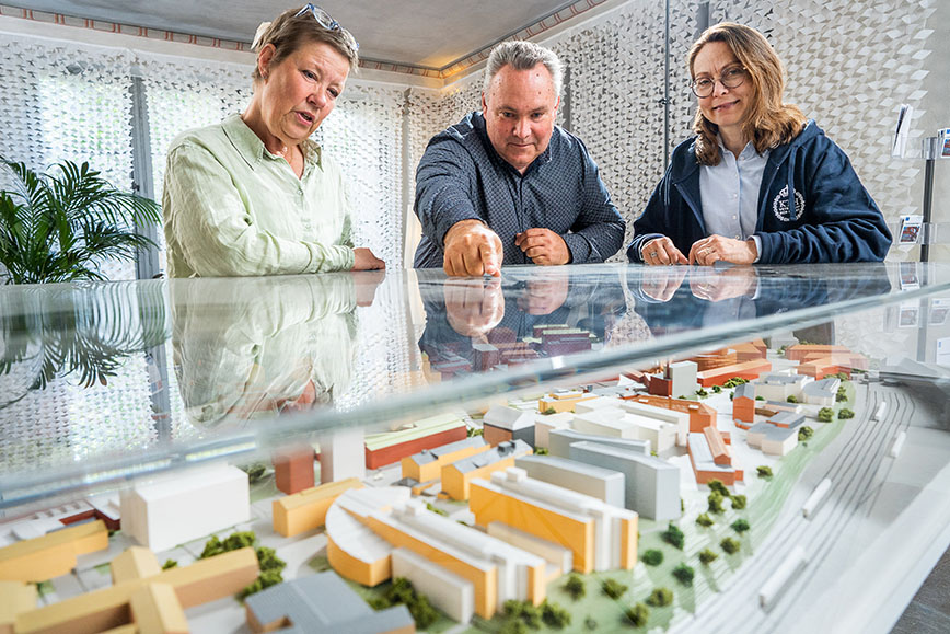 Two women and a man stand leaning over a glass case. In the stand there is a model of the KTH Campus