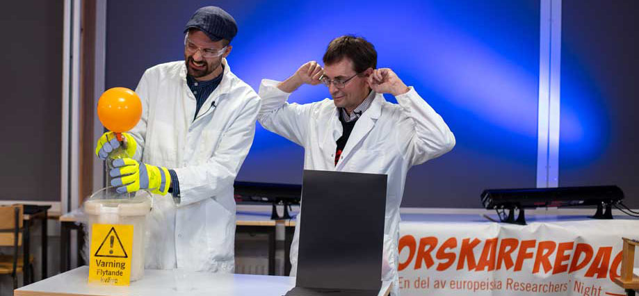 Två forskare som utför ett experiment i vita rockar. En håller för öronen.