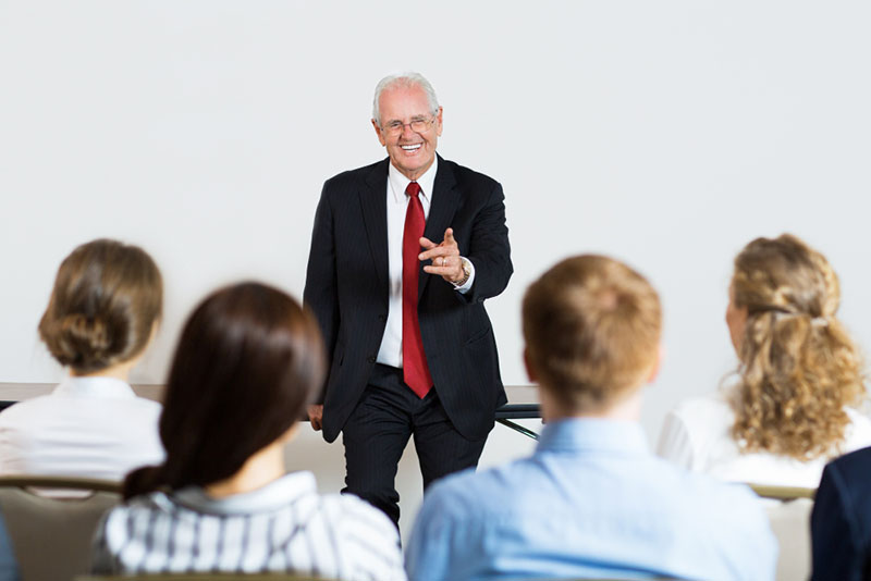 En äldre man i en röd slips som pratar med studenter