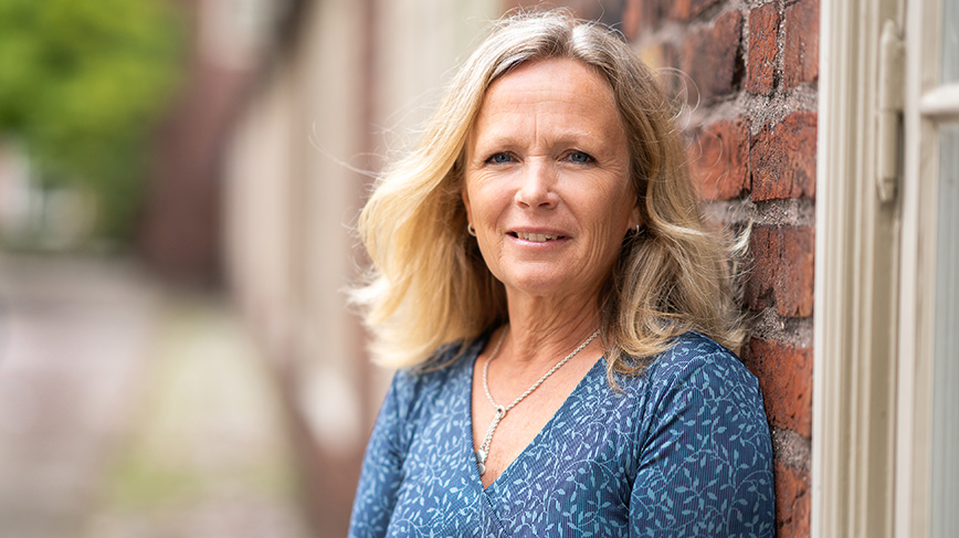 Kvinna mot mur i blå klänning.