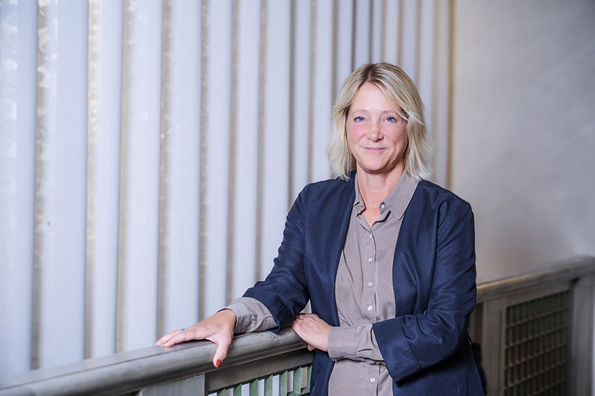 Porträttfoto: en blond kvinna i blå kavaj framför ett ljust draperi.