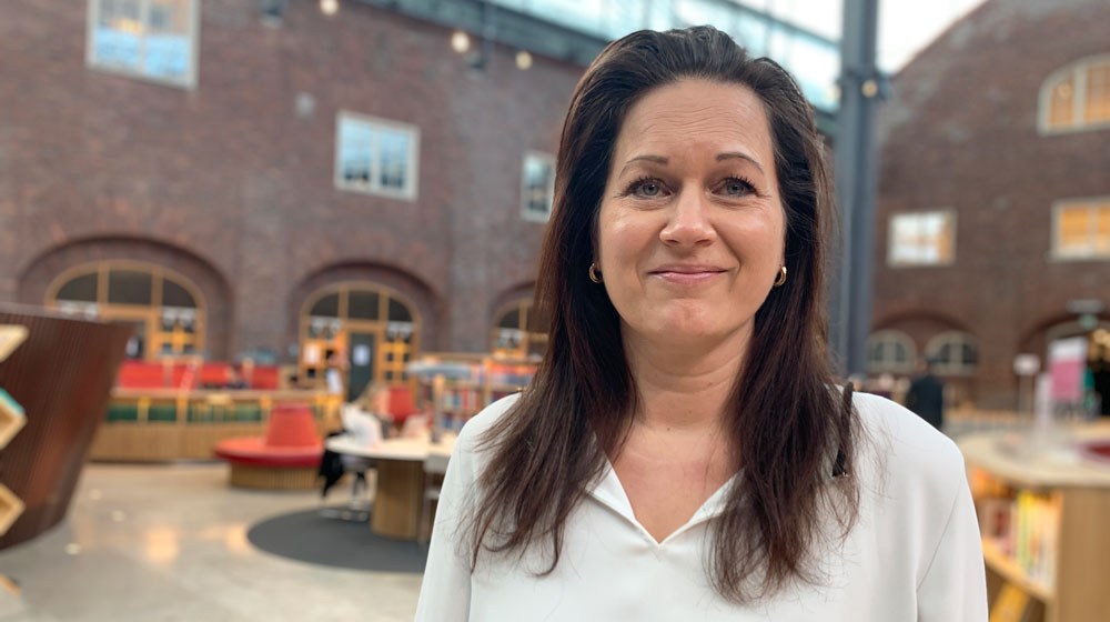 Photo: Smiling woman wearing a white shirt in KTH's open library environment.