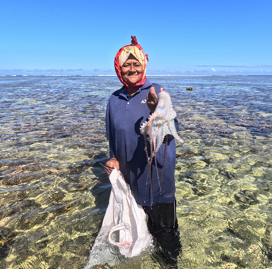 A woman standing in shallow water holding an octopus