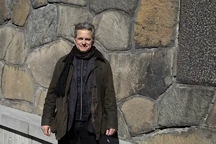 Man standing leaning against a stone wall.