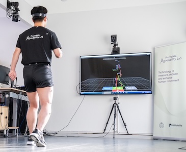 Man with markers standing in front of multiple cameras and a screen with his pose visualized