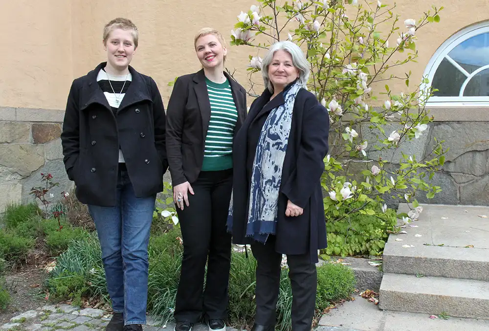 Three people standing in front of wall and magnolia.
