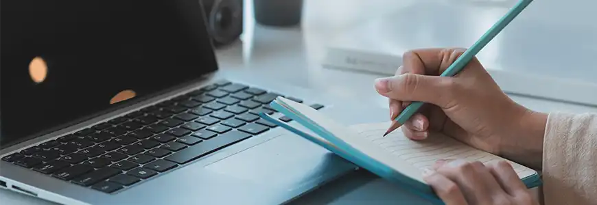 A hand with a pen, a notebook and a laptop computer