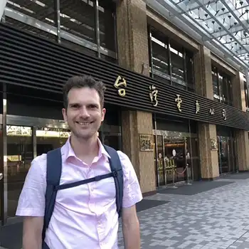 A man in a pink short sleeved shirt in front of a building with asiatic signs on it