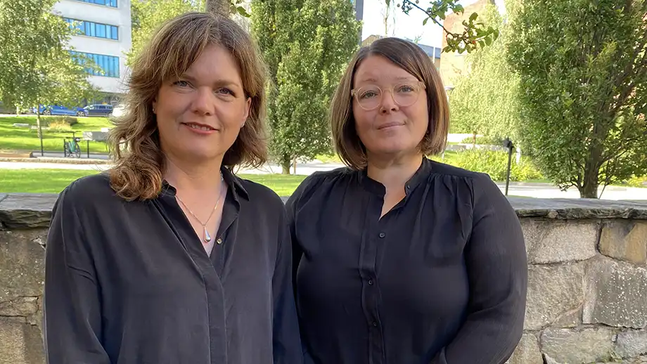Två kvinnor i svarta skjortor framför stenmur.