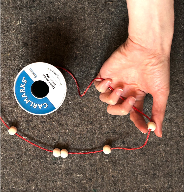 Hand med rött band och pärlor