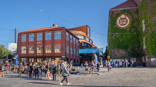 Photo: student groups in front of two KTH buildings, blue sky.
