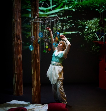 Hannah in white dress reaches up to touch a wind chime made of CDs