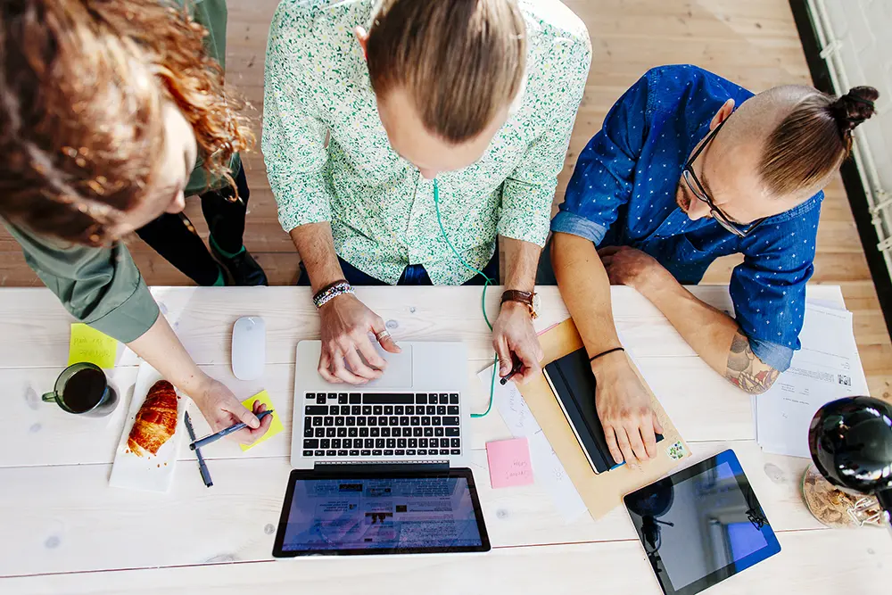 Three persons sitting at a table with office supplies and a laptop
