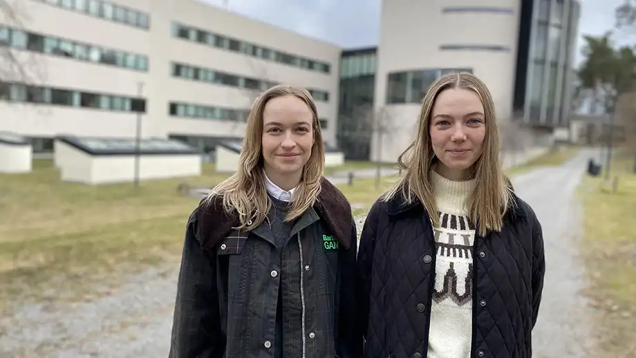 Två kvinnor framför vita byggnader. 