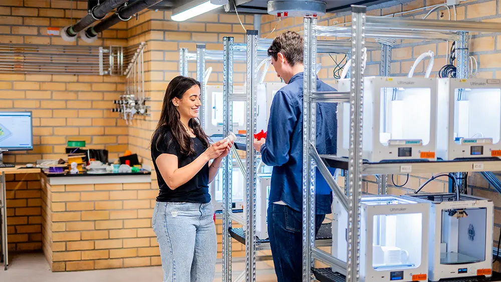 Två studenter i en makermiljö fylld med 3d-skrivare på KTH.