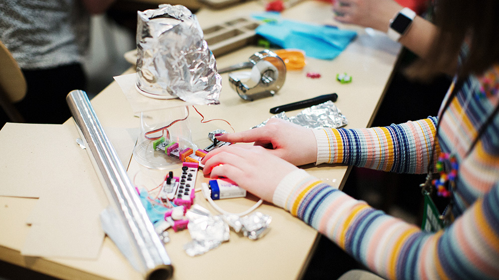 En ung tjej sitter vid ett bord och bygger en teknisk lösning med hjälp av olika komponenter.