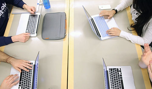 People and hands at a table with laptops.
