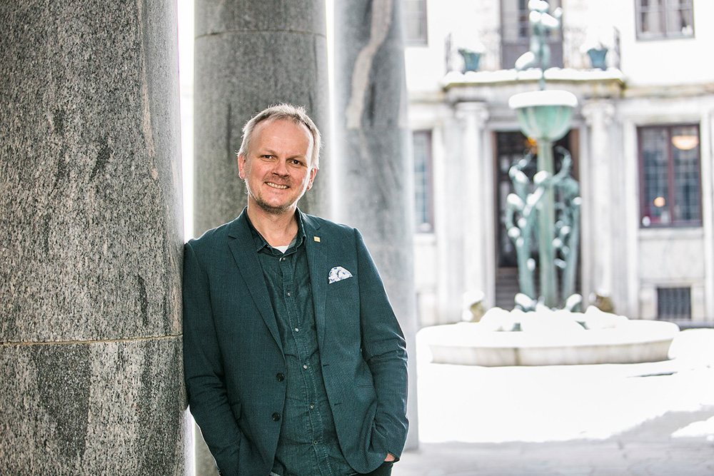Jan Gulliksen is standing in an arch outdoors on KTH Campus. In the background, a sculpture can be seen.